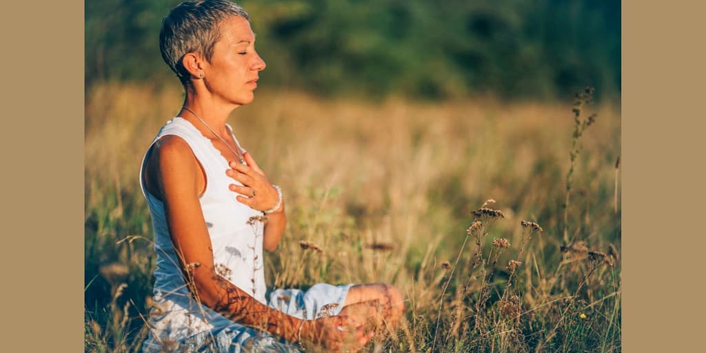 8 powerful and amazing mindfulness energy techniques woman meditating in field.