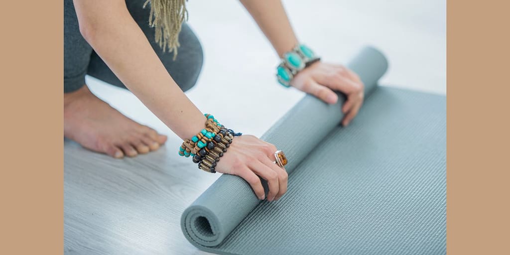 Holistic living path top 6 supreme yoga mats from amazon and they're importance for a well-rounded practice image of a woman rolling a light blue yoga mat..