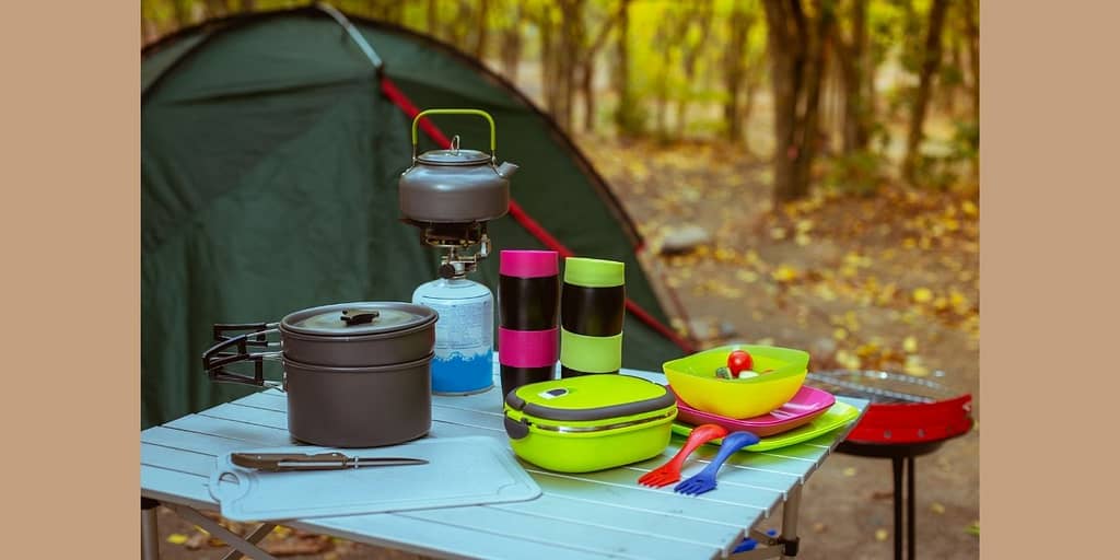 Camping and kitchen gear on the table next to a tent.